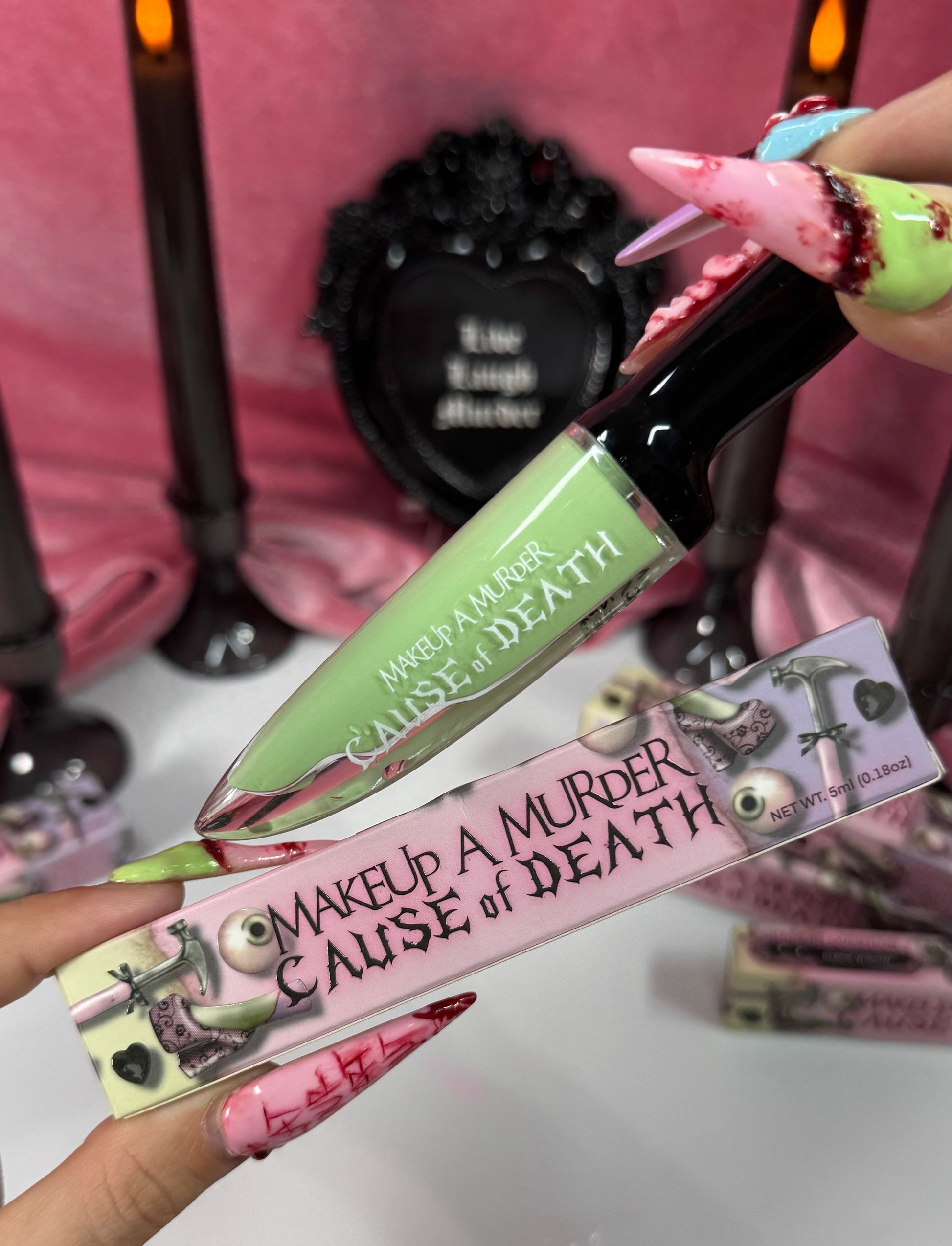 Makeup product with 'Makeup a Murder Cause of Death' text held by a person with colorful nails.